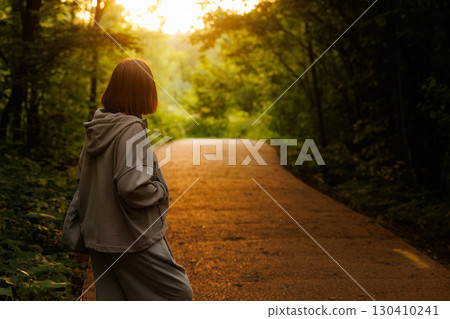 Woman enjoying a quiet moment on a forest path during sunset near a tranquil wooded area Woman enjoying a quiet moment on a forest path during sunset near a tranquil wooded area 130410241