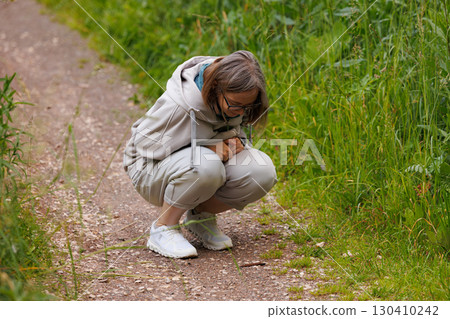Person squatting on a path in a green field observing nature with curiosity in early afternoon light 130410242