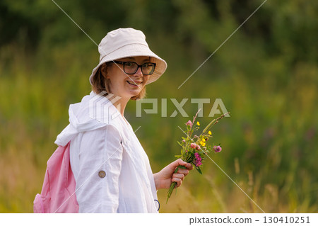 Smiling young woman holding wildflowers in a green meadow during a sunny day in summer Smiling young woman holding wildflowers in a green meadow during a sunny day in summer 130410251