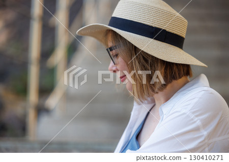 Woman relaxing outdoors wearing a straw hat and glasses near steps during a sunny day Woman relaxing outdoors wearing a straw hat and glasses near steps during a sunny day 130410271