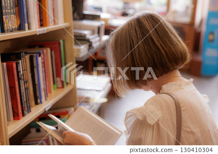 Woman browsing through books in a cozy library during a quiet afternoon 130410304