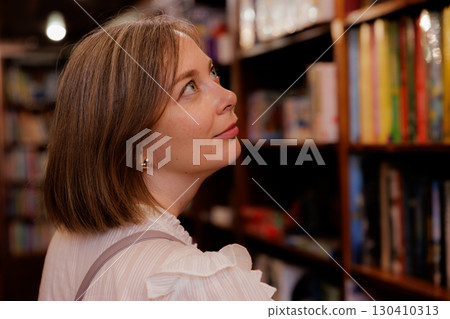 Woman exploring bookshelves in a cozy library setting during a quiet afternoon 130410313