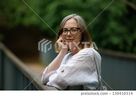 Woman posing thoughtfully on a wooden railing in a lush green outdoor setting during the daytime Woman posing thoughtfully on a wooden railing in a lush green outdoor setting during the daytime 130410314