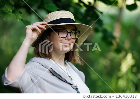 Woman wearing a straw hat in a lush green setting during daylight hours Woman wearing a straw hat in a lush green setting during daylight hours 130410318