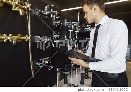 Salesman working in construction market standing with water taps near the showcase of plumbing shop Salesman working in construction market standing with water taps near the showcase of plumbing shop 130411052