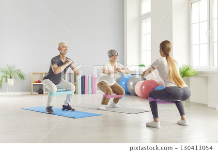 Elderly mature people group exercising with rubber band with fitness trainer in gym. Elderly mature people group exercising with rubber band with fitness trainer in gym. 130411054