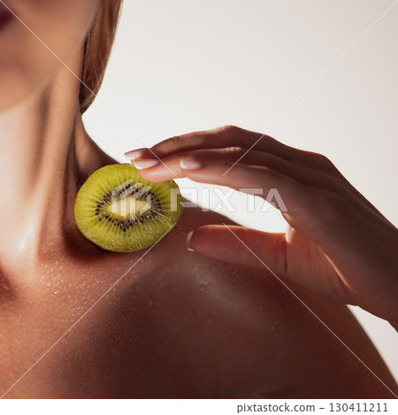 Woman with kiwi slice on shoulder in clean wellness aesthetic Woman with kiwi slice on shoulder in clean wellness aesthetic 130411211