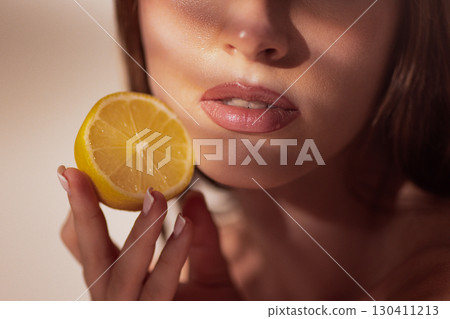 Woman face with lemon slice held near lips in artistic wellness concept 130411213
