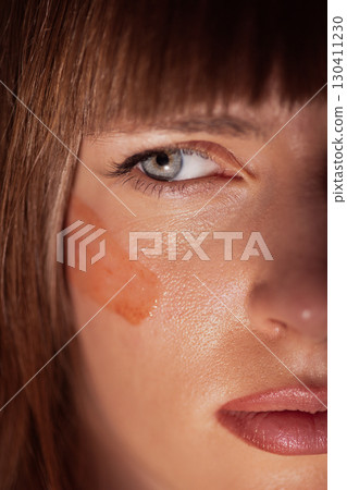 Woman face closeup with red clay mask applied under eye for skincare Woman face closeup with red clay mask applied under eye for skincare 130411230
