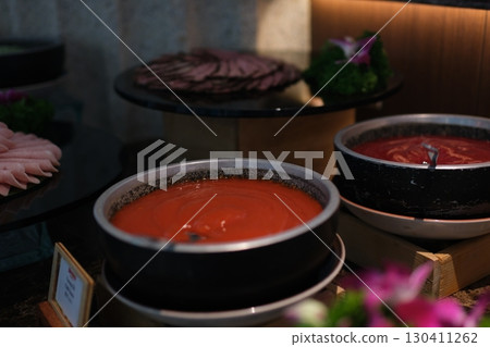 High Angle View of Various Comforting and Savory Gourmet Soups Served in Bread Bowls and Handled Dishes and Topped with Variety of Garnishes on Table Surface with Gray Tablecloth 130411262