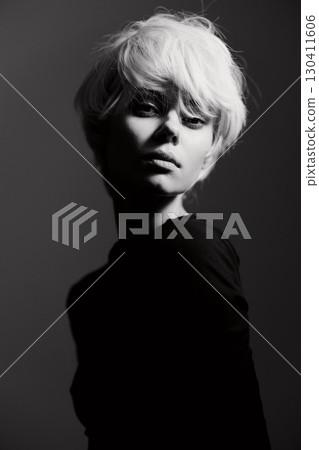 Thoughtful young woman with short light hair posing in a dramatic black and white portrait, exuding confidence and artistic expression. 130411606