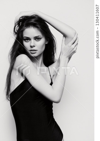 Black and white portrait of a confident woman with long hair, posing with a sensual expression and elegant posture against a neutral backdrop. 130411607