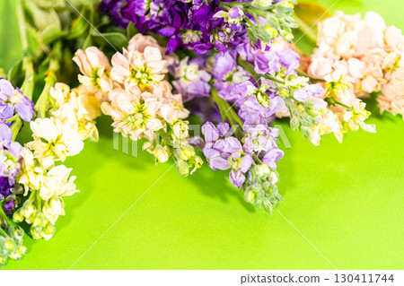 A vibrant flat lay of assorted stock flowers in soft pink, pale yellow, lavender, and deep purple, arranged against a vivid green backdrop. The image highlights the contrast between the pastel floral A vibrant flat lay of assorted stock flowers in soft pink, pale yellow, lavender, and deep purple, arranged against a vivid green backdrop. The image highlights the contrast between the pastel floral 130411744