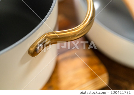 Closeup of a ceramic pot with a golden side handle and a smooth grey nonstick interior, resting on a rustic wood counter. 130411781