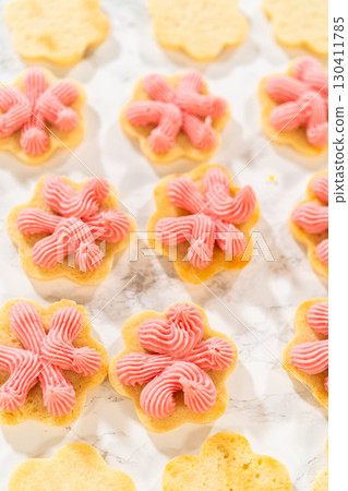 Vertical layout of flower-shaped cookies topped with piped raspberry buttercream, ready to be sandwiched for Easter Cookie Sandwich with Raspberry Buttercream. 130411785