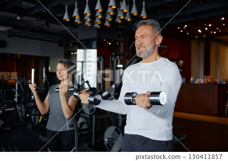 Mature couple are lifting heavy dumbbells in a gym setting Mature couple are lifting heavy dumbbells in a gym setting 130411857