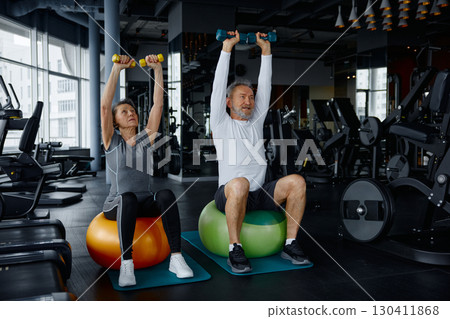 Mature couple sit on exercise balls in a gym with dumbbells 130411868