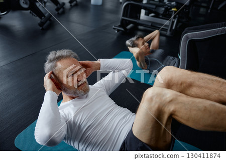 Man is performing sit ups on a workout mat inside a gym facility 130411874