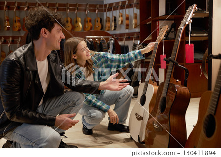 A man and a girl are happily looking at various guitars in a store A man and a girl are happily looking at various guitars in a store 130411894