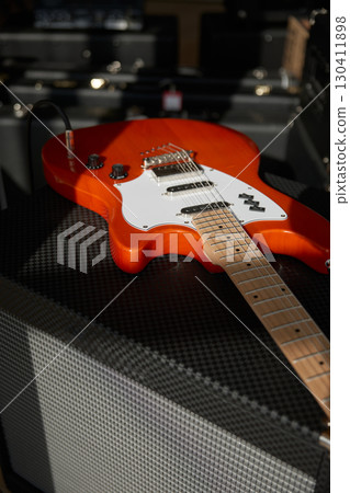 An orange electric guitar on top of a powerful amplifier 130411898