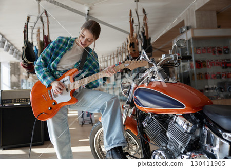 A woman plays guitar while sitting on a motorcycle A woman plays guitar while sitting on a motorcycle 130411905