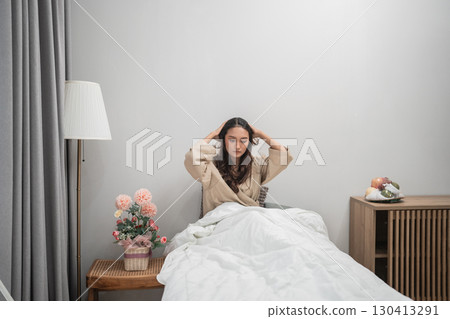 A stressed woman lying in bed is surrounded by minimalist, contemporary decor 130413291