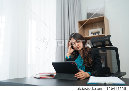 A stressed businesswoman is intensely working on a tablet in a modern office setting A stressed businesswoman is intensely working on a tablet in a modern office setting 130413536