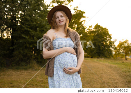 Pregnant woman holding baby bump outdoors in sunset light 130414012