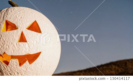 Unusual white Halloween pumpkin with carved smiling face on countryside field with clear evening sky background 130414117