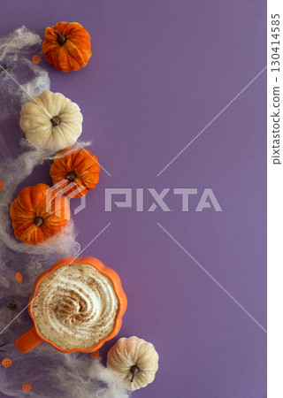Halloween themed flat lay with a pumpkin latte, decorative pumpkins and spiderwebs on a purple background. 130414585