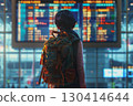 Smiling young woman in an airport terminal looking at her phone, with a backpack on her shoulder and a flight information display board in the blurry background 130414644