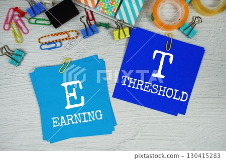 ET - Earning Threshold text on stick note with stationery on concrete background ET - Earning Threshold text on stick note with stationery on concrete background 130415283