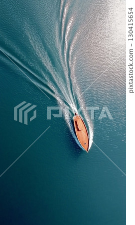 Aerial view of a luxury wooden yacht sailing on calm turquoise water leaving a wake behind, with the sun reflecting on the surface, creating a luxurious and relaxing holiday atmosphere 130415654