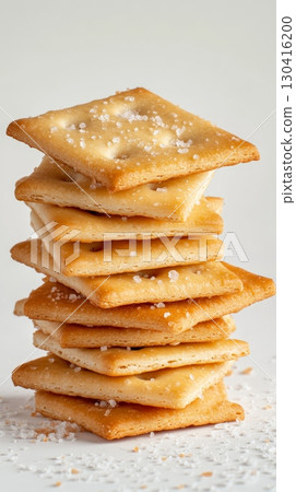 Square crackers forming a tall stack on a white surface, with visible salt crystals enhancing their savory appeal and suggesting a crispy texture Square crackers forming a tall stack on a white surface, with visible salt crystals enhancing their savory appeal and suggesting a crispy texture 130416200