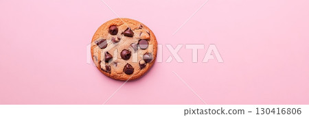 Freshly baked chocolate chip cookie resting on a vibrant pink backdrop, showcasing its golden brown texture and rich chocolate chips, creating a visually appealing treat for dessert lovers 130416806
