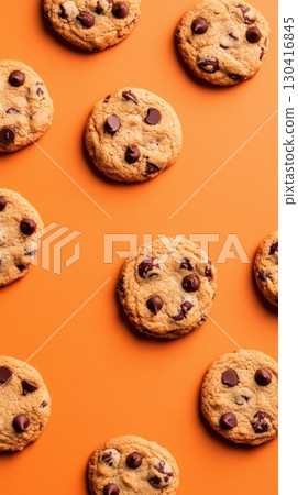 Pattern of golden brown chocolate chip cookies spread out on a vibrant orange surface, creating a visually appealing arrangement for food and dessert lovers 130416845