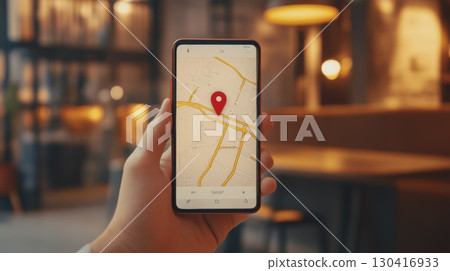 Businessman holding a smartphone with a navigation app displaying a red pin on an online map, indicating a specific location in a restaurant or nearby area 130416933