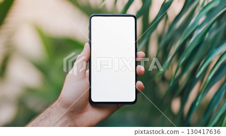 Close up of a hand holding a modern smartphone with a blank white screen, perfect for showcasing your app or website design against a lush tropical garden background Close up of a hand holding a modern smartphone with a blank white screen, perfect for showcasing your app or website design against a lush tropical garden background 130417636