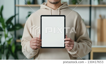 Close up of a man holding a digital tablet with a blank white screen, providing a space for designers to showcase their work in a realistic setting 130417653