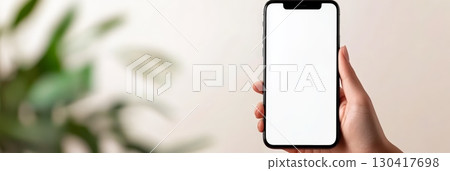 Woman holding a modern smartphone featuring a blank white screen, set against a backdrop of blurred plants, ideal for displaying mobile app or website design concepts 130417698