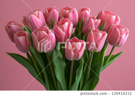 A beautiful fresh bouquet of vibrant pink tulips with green stems and leaves. Many colorful flowers bloom against a soft pastel pink background. 130418152