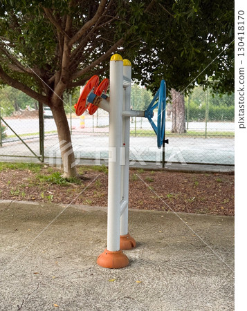 Outdoor training machine located near tennis court in park. Fitness, movement, and wellness showing community activity, strength, and health in daily lifestyle. Outdoor training machine located near tennis court in park. Fitness, movement, and wellness showing community activity, strength, and health in daily lifestyle. 130418170
