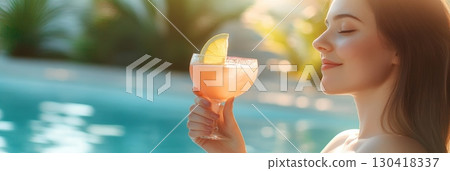 Young woman holding a refreshing cocktail by the poolside, enjoying the summer sun and tropical ambiance during her vacation at a luxurious resort 130418337