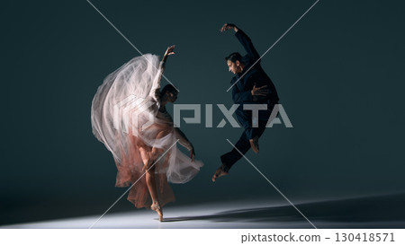 Ballet couple moving in synchronized dramatic jump with flowing dress motion 130418571
