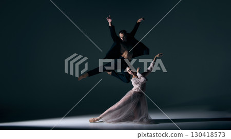 Male dancer soaring midair while female partner kneels in expressive pose 130418573