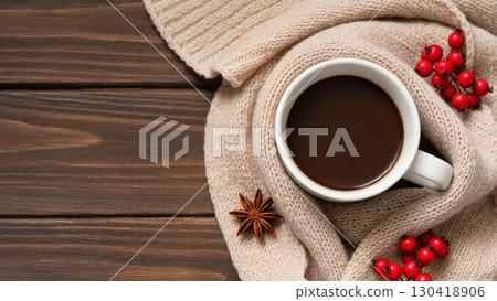 Christmas cup of hot chocolate wrapped in knitted scarf with red berries and anise on wooden table. Cozy winter composition. 130418906