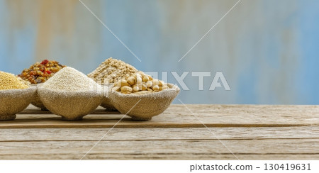 Various grains and seeds in small burlap sacks rest on a rustic wooden table against a blurred blue background Various grains and seeds in small burlap sacks rest on a rustic wooden table against a blurred blue background 130419631
