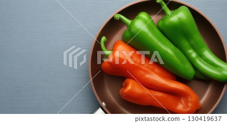 Three bell peppers, one orange and two green, rest in a copper frying pan on a gray surface Three bell peppers, one orange and two green, rest in a copper frying pan on a gray surface 130419637