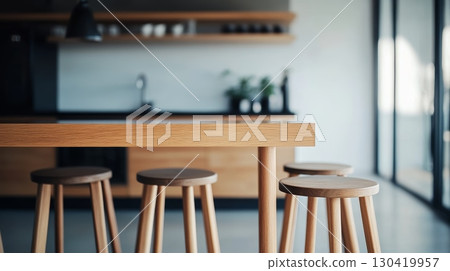 Natural light illuminates a contemporary kitchen featuring a sleek wooden table and matching stools, creating a warm and inviting atmosphere perfect for modern living 130419957