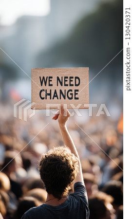 Activist holding a cardboard sign reading we need change during a bustling protest march, advocating passionately for vital political and social reforms in the community 130420371